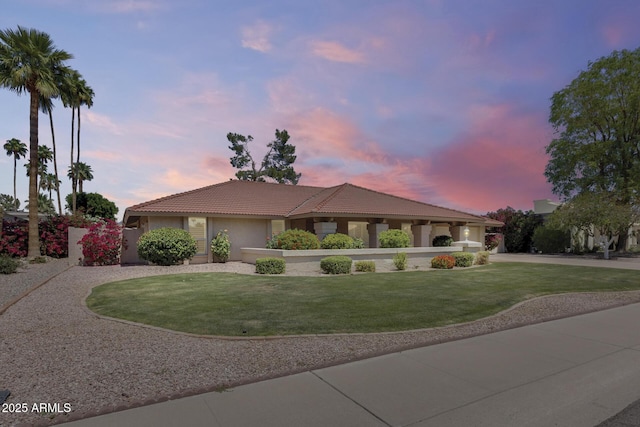 view of front of property with a yard, an attached garage, stucco siding, a tile roof, and curved driveway