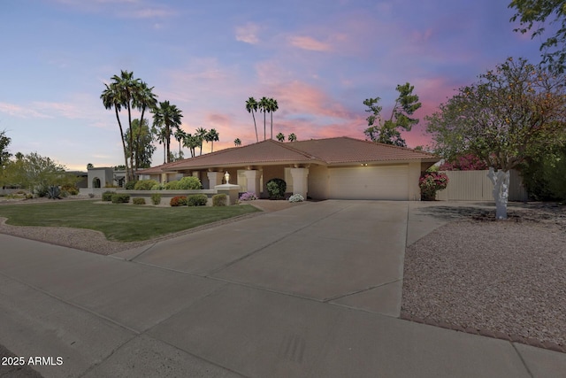 ranch-style home with an attached garage, a tiled roof, fence, concrete driveway, and a yard