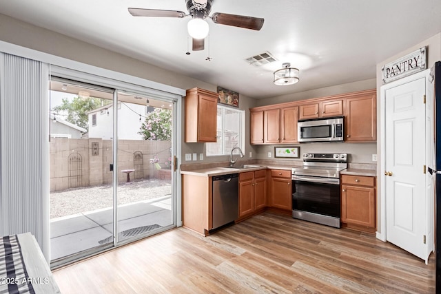 kitchen featuring appliances with stainless steel finishes, a sink, light countertops, light wood finished floors, and ceiling fan