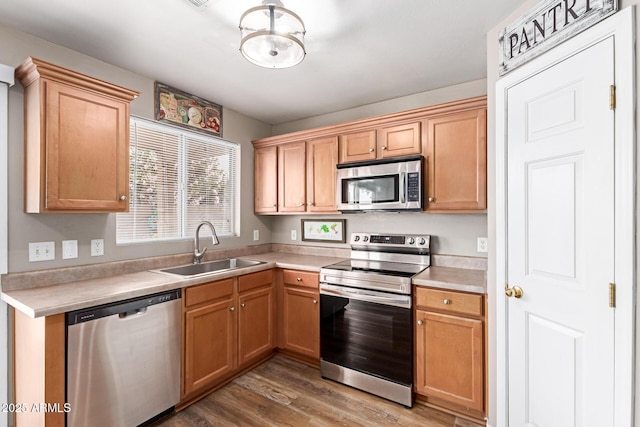 kitchen with stainless steel appliances, a sink, light wood-style flooring, and light countertops