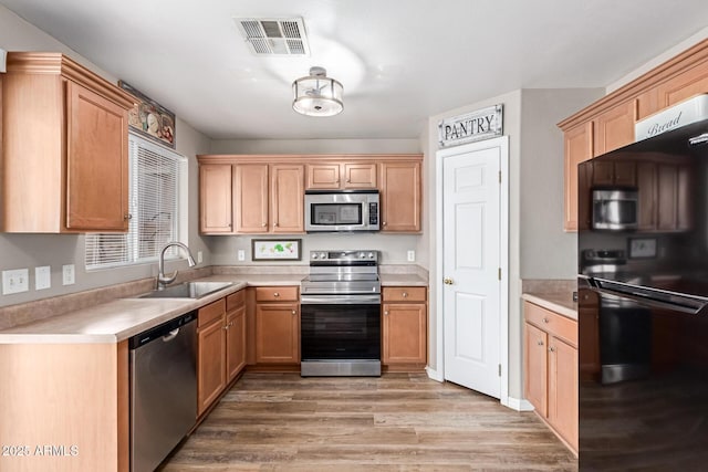 kitchen featuring appliances with stainless steel finishes, a sink, light countertops, and light wood-style floors