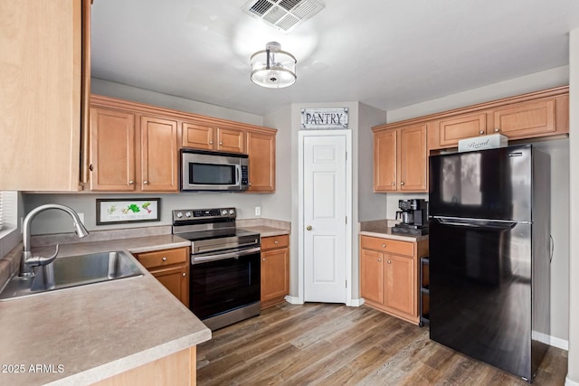 kitchen featuring appliances with stainless steel finishes, a sink, wood finished floors, light countertops, and baseboards
