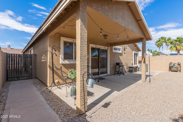 rear view of property with stucco siding, a gate, fence, and a patio area
