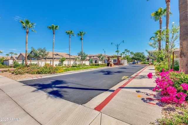 view of asphalt road with a residential view, street lights, and curbs