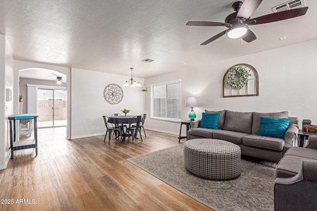 living room featuring a ceiling fan, light wood-style flooring, baseboards, and arched walkways
