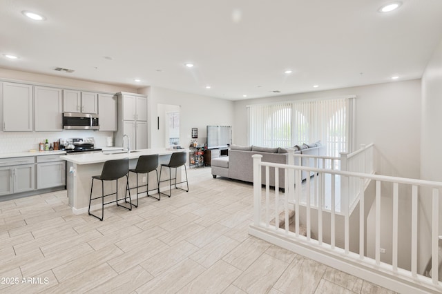 155 N Lakeview Blvd Unit 268, Chandler, AZ 85225 - kitchen featuring stainless steel appliances, gray cabinetry, a sink, a kitchen island with sink, and tasteful backsplash