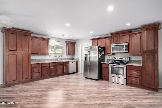 kitchen with appliances with stainless steel finishes, light wood-type flooring, a sink, and recessed lighting