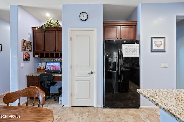 kitchen featuring light stone counters, black fridge, built in desk, and decorative backsplash