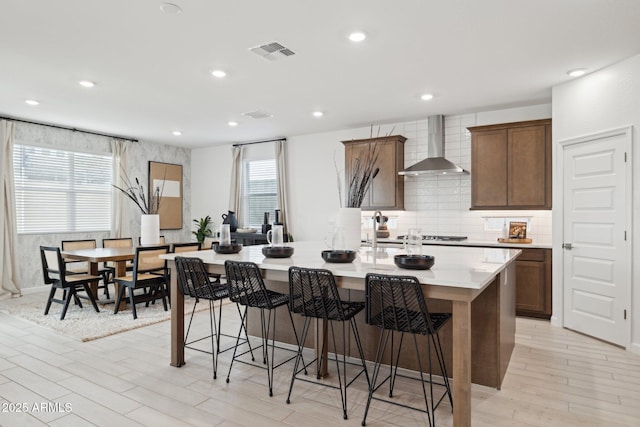 7333 W Buckhorn Trl, Peoria, AZ 85383 - kitchen featuring wall chimney exhaust hood, an island with sink, a kitchen bar, light wood finished floors, and backsplash