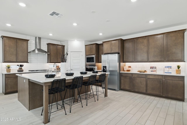 7333 W Buckhorn Trl, Peoria, AZ 85383 - kitchen featuring stainless steel appliances, wall chimney exhaust hood, backsplash, light wood-style floors, and an island with sink