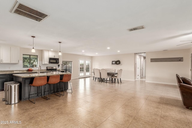 kitchen featuring light stone countertops, pendant lighting, white cabinets, stainless steel range, and a center island with sink