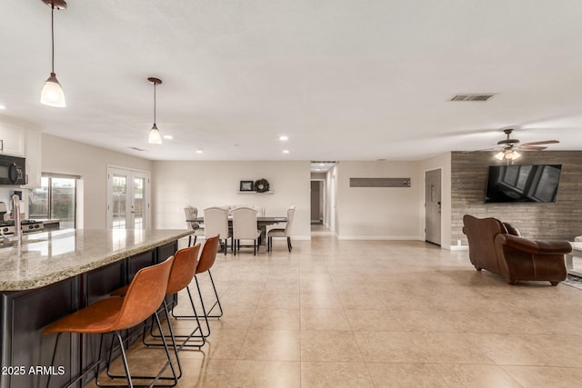 kitchen featuring a kitchen bar, ceiling fan, hanging light fixtures, light stone countertops, and white cabinets