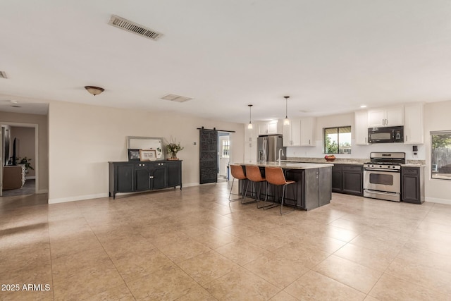 kitchen with a barn door, stainless steel appliances, hanging light fixtures, white cabinets, and a center island