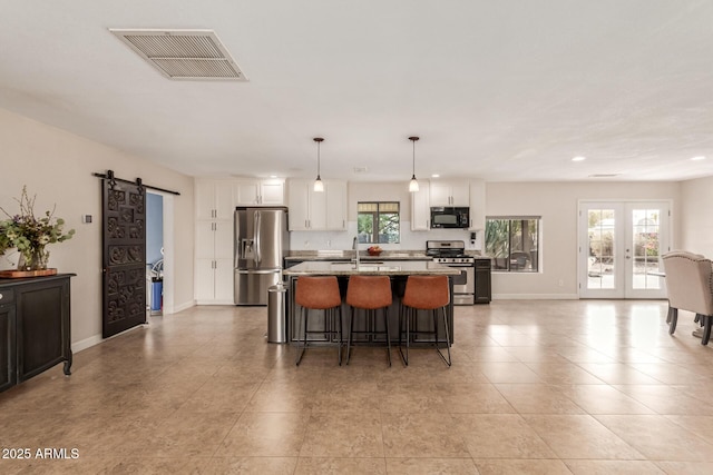 kitchen with white cabinetry, a barn door, stainless steel appliances, decorative light fixtures, and light stone counters