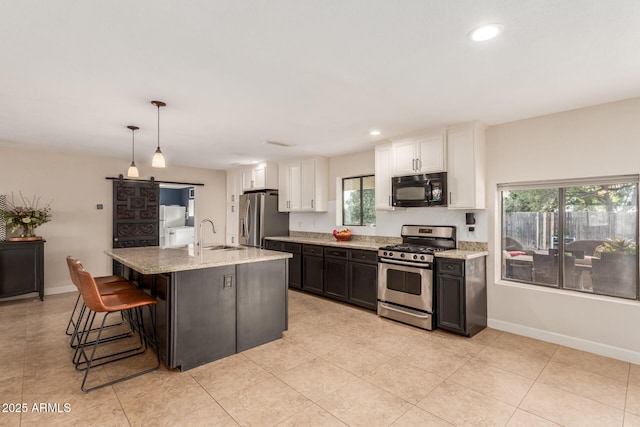 kitchen with white cabinets, decorative light fixtures, stainless steel appliances, a kitchen island with sink, and a barn door