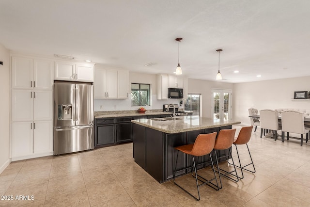 kitchen with a center island with sink, stainless steel appliances, light stone countertops, pendant lighting, and white cabinets