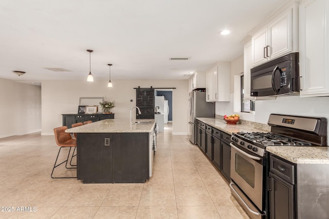 kitchen featuring a barn door, a center island with sink, appliances with stainless steel finishes, hanging light fixtures, and white cabinets