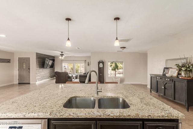 kitchen with light stone countertops, ceiling fan, hanging light fixtures, and sink