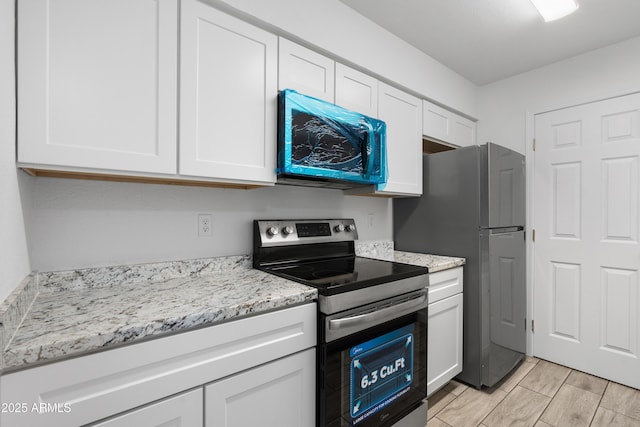 kitchen featuring appliances with stainless steel finishes, wood finish floors, white cabinets, and light stone countertops