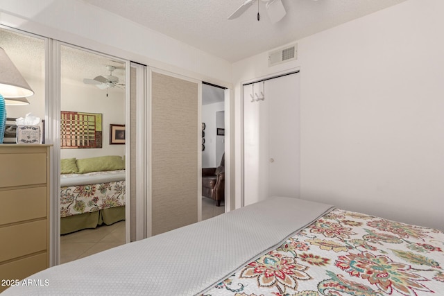 tiled bedroom featuring a textured ceiling, a closet, visible vents, and a ceiling fan