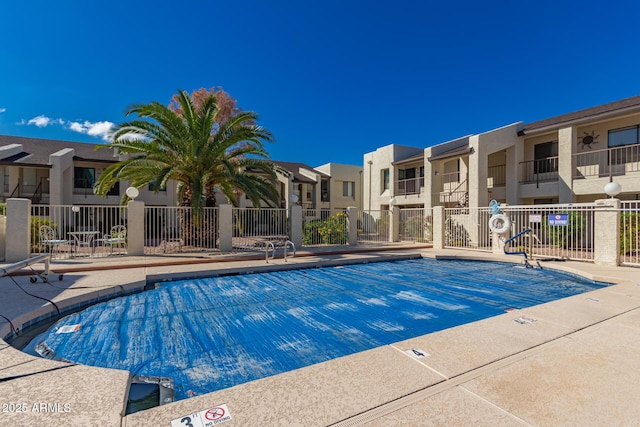 community pool with a patio, fence, and a residential view