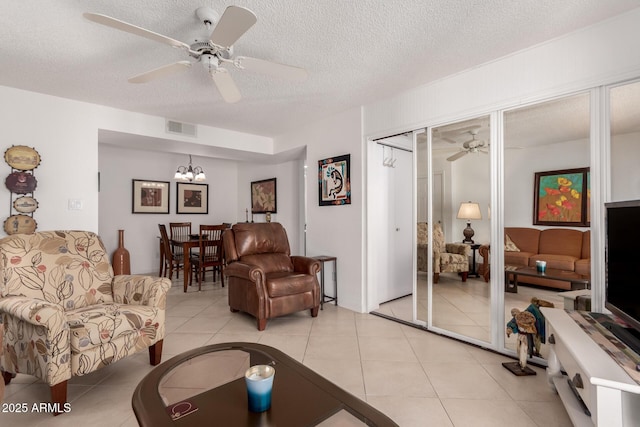 living room with ceiling fan with notable chandelier, visible vents, a textured ceiling, and light tile patterned floors