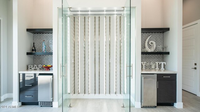 kitchen featuring premium appliances, wall chimney range hood, white cabinetry, light stone countertops, and decorative backsplash