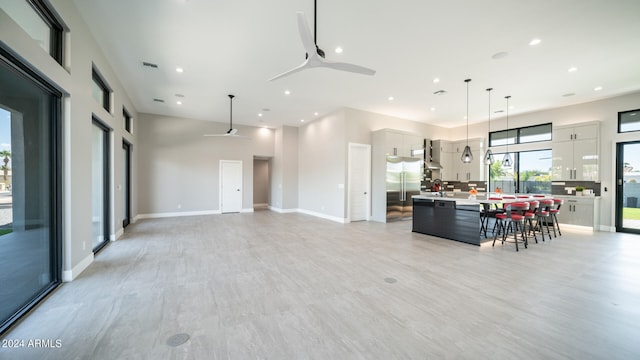 kitchen with an island with sink, white cabinets, hanging light fixtures, high quality fridge, and ceiling fan