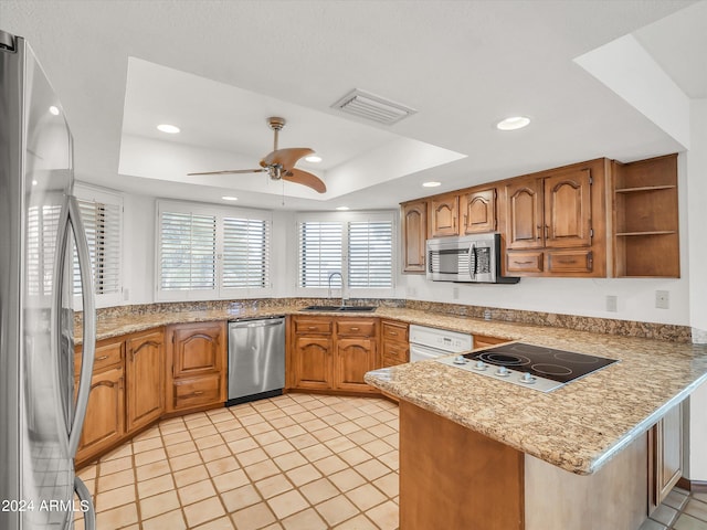 kitchen with kitchen peninsula, ceiling fan, sink, stainless steel appliances, and a raised ceiling