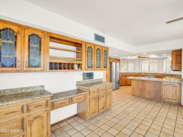 kitchen featuring kitchen peninsula, stainless steel fridge, ceiling fan, light stone counters, and light tile flooring