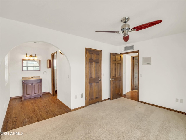 unfurnished bedroom featuring ceiling fan, ensuite bath, and dark colored carpet