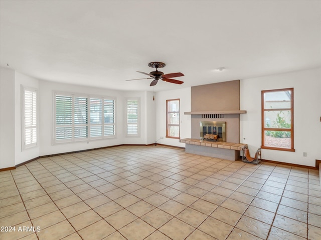 unfurnished living room with a fireplace, light tile floors, ceiling fan, and plenty of natural light