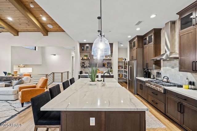 kitchen with visible vents, appliances with stainless steel finishes, a sink, light wood-style floors, and wall chimney exhaust hood