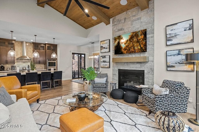living room featuring a fireplace, beamed ceiling, light wood-style floors, wooden ceiling, and a ceiling fan