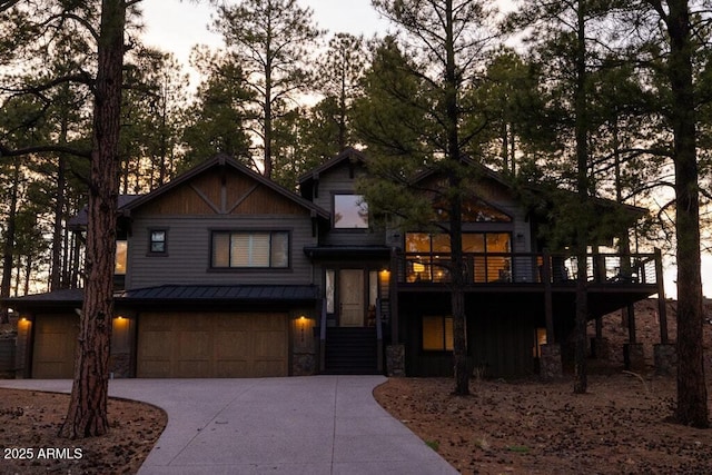 view of front of house with a standing seam roof, a wooden deck, a garage, concrete driveway, and stone siding