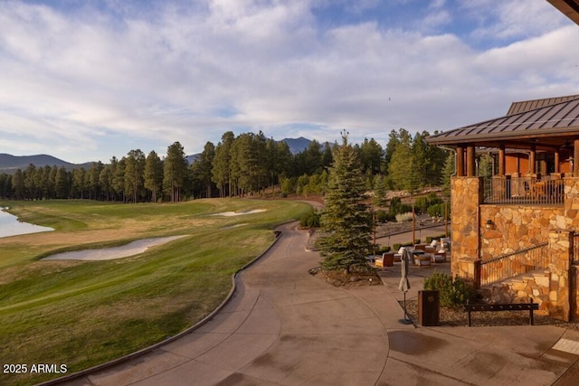 view of community featuring a yard, a view of trees, view of golf course, and a mountain view