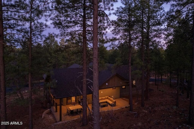 exterior space featuring a view of trees, a patio, and a shingled roof