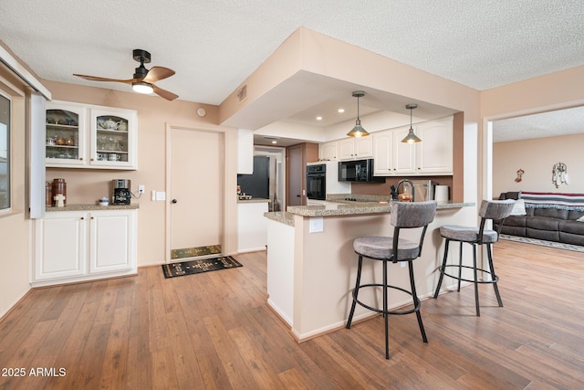 kitchen featuring white cabinetry, light stone countertops, a textured ceiling, decorative light fixtures, and black appliances