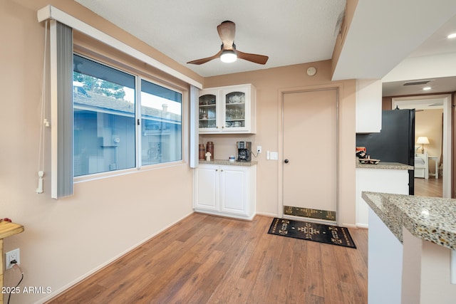 kitchen featuring ceiling fan, light stone countertops, white cabinetry, and light wood-type flooring