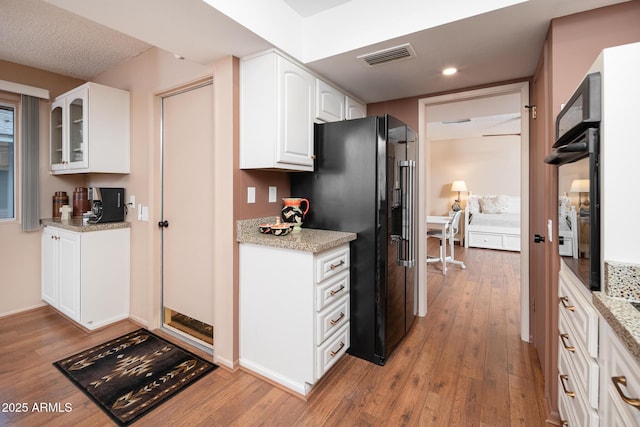 kitchen featuring white cabinets, black refrigerator, light stone counters, and light hardwood / wood-style flooring