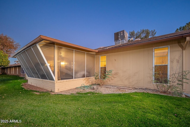 property exterior at dusk with a sunroom, central AC unit, and a yard