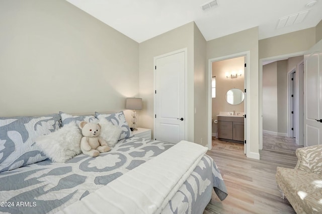 bedroom with ensuite bathroom, light hardwood / wood-style flooring, and sink