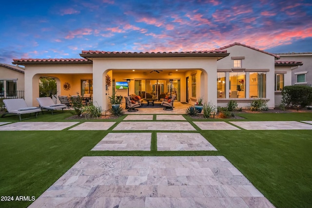 back house at dusk featuring a lawn, a patio area, an outdoor living space, and ceiling fan