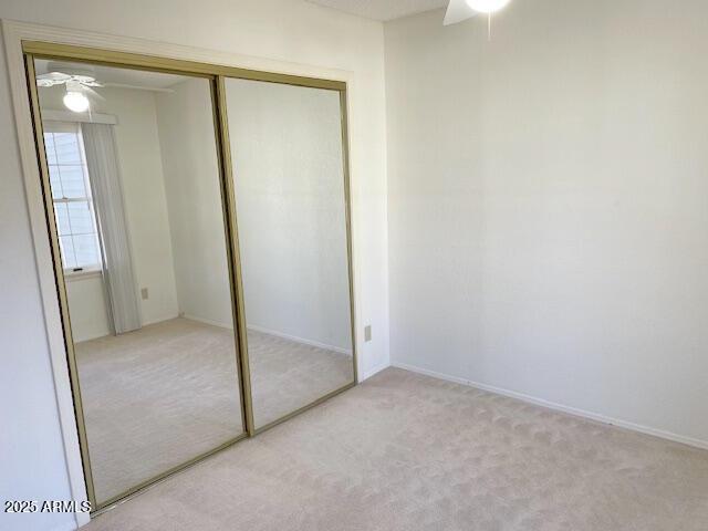 unfurnished bedroom with ceiling fan, light carpet, and a closet