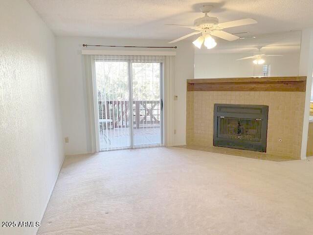 unfurnished living room featuring carpet flooring, ceiling fan, a fireplace, and a textured ceiling