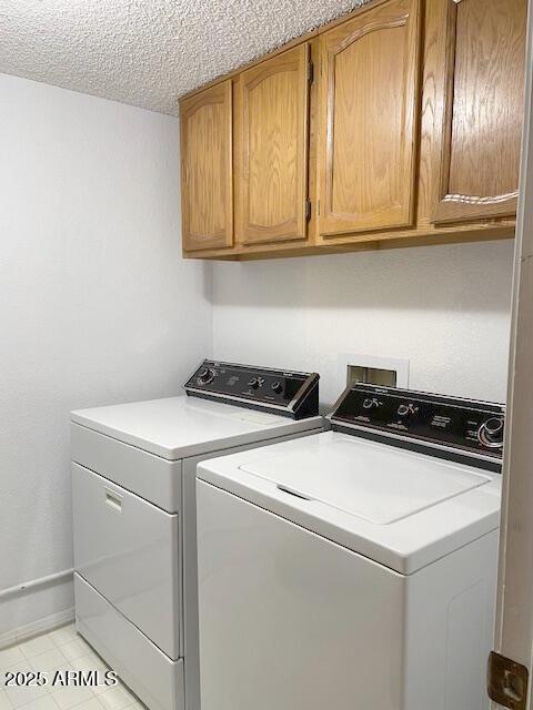 clothes washing area with cabinets, washing machine and dryer, and a textured ceiling