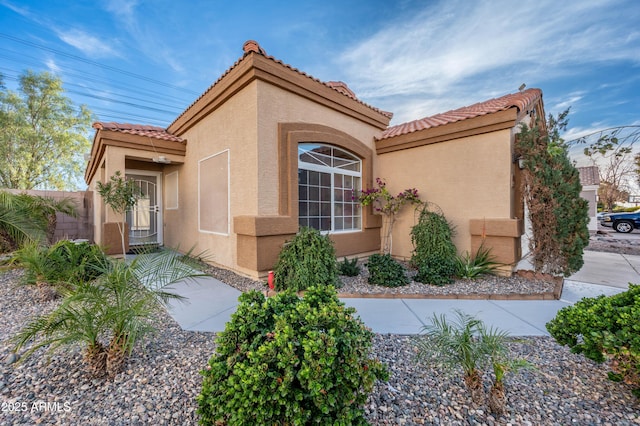 view of property exterior with a tiled roof, fence, and stucco siding