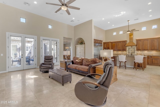 tiled living room with ceiling fan, french doors, and a high ceiling