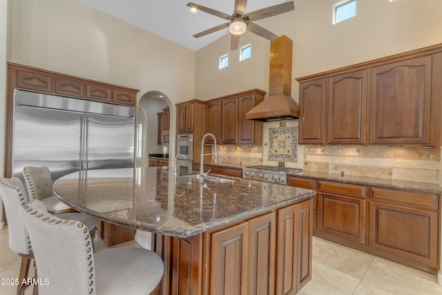 kitchen featuring custom exhaust hood, a kitchen island with sink, dark stone counters, and a high ceiling