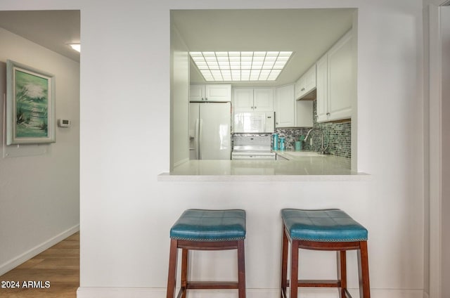 kitchen featuring kitchen peninsula, white appliances, white cabinets, hardwood / wood-style floors, and a breakfast bar area